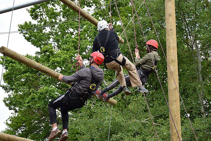 3 Erwachsene Teilnehmer*innen schaukeln im Hochseilgarten